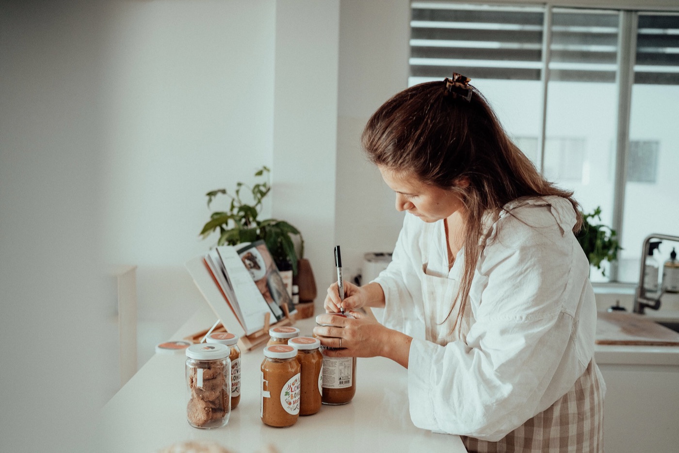 Leila labelling jars of nourishing food at her kitchen bench